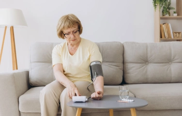 женщина сидит на диване дома и измеряет давление