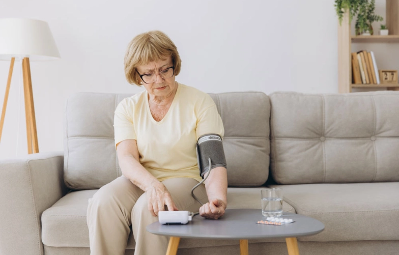 женщина сидит на диване дома и измеряет давление